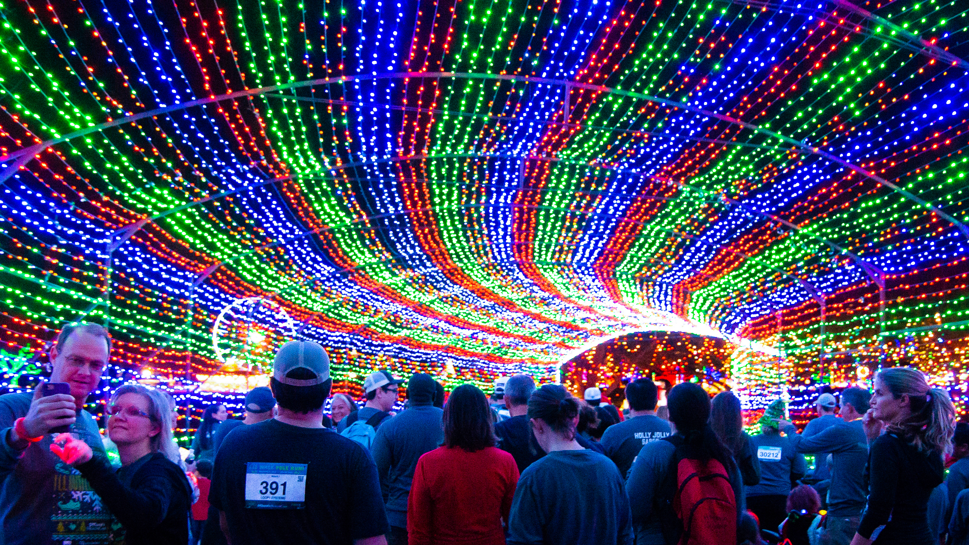 A crowd of people under a holiday light display